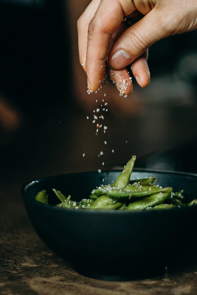 Hand sprinkeling sesame seeds on Edamame beans
